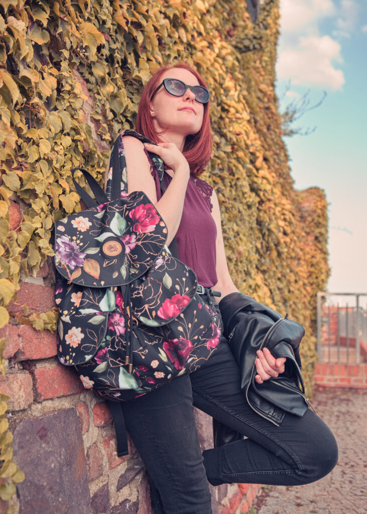 Žena opřená o zeď s dámským květovaným batohem ELLIE Od Klárky na zádech